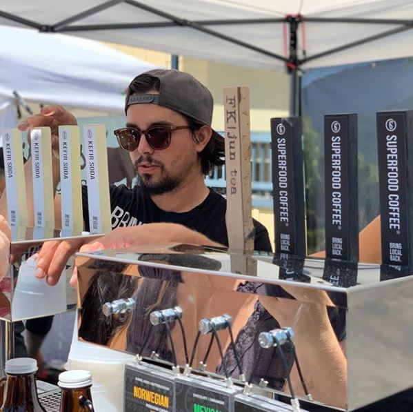 A man stands behind beverage taps at a local farmers' market