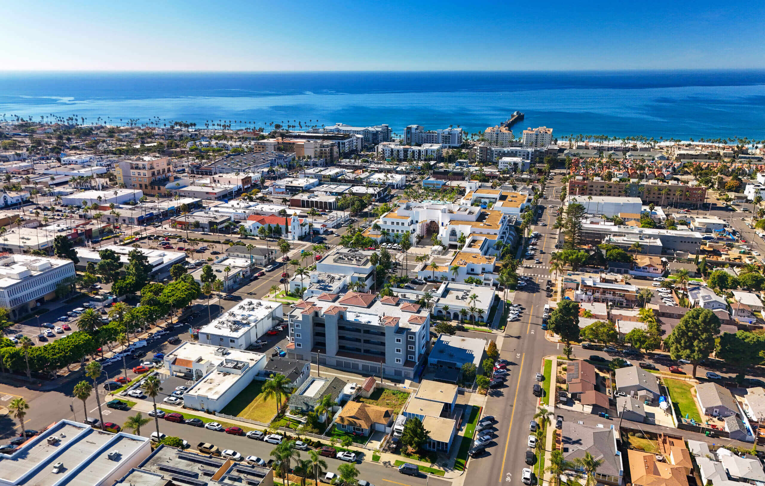 Aerial of Oceanside, CA in the San Diego metropolitan area, with a view of the Pacific Ocean and a clear blue sky in the background.