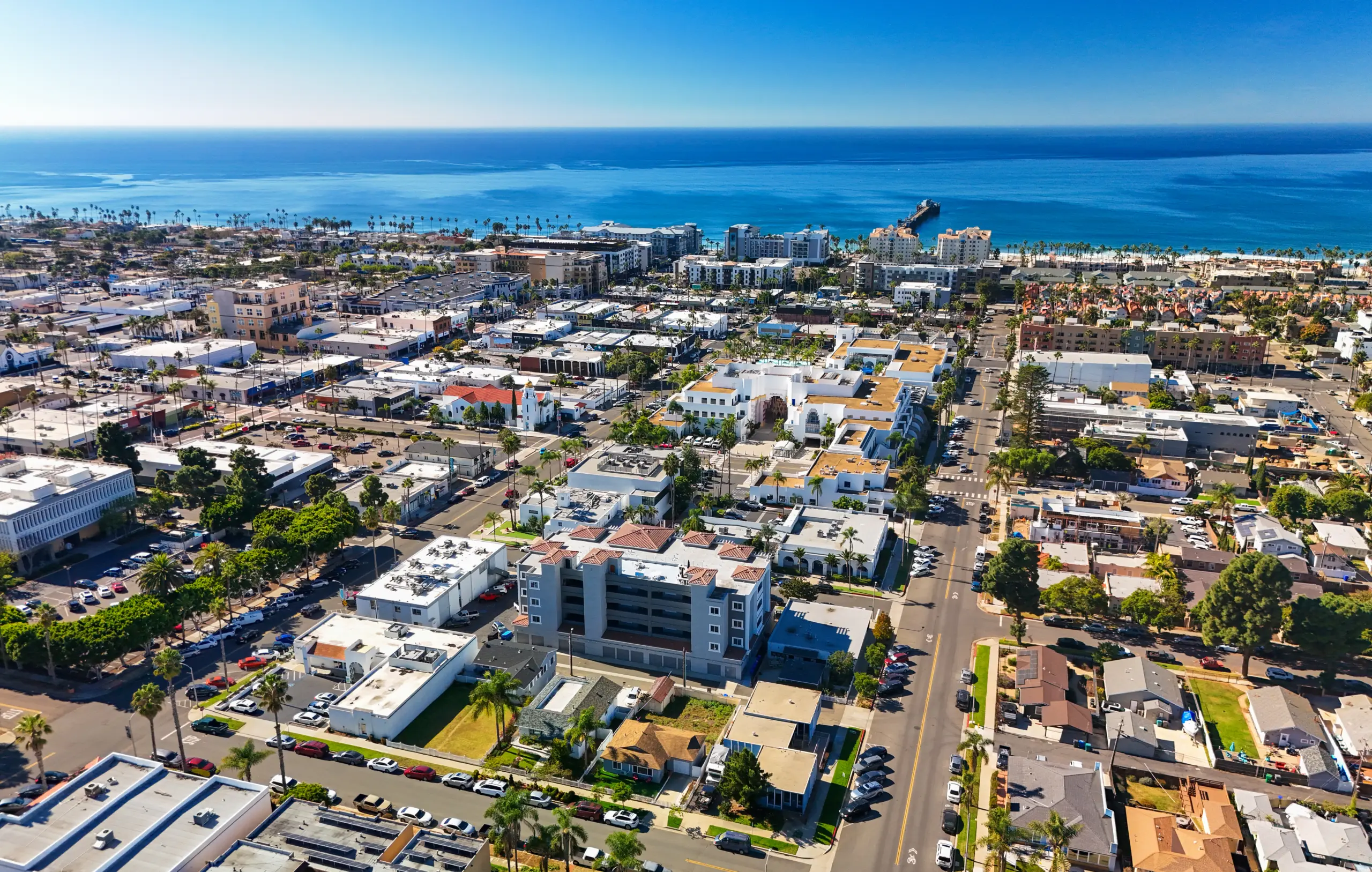 Aerial of Oceanside, CA in the San Diego metropolitan area, with a view of the Pacific Ocean and a clear blue sky in the background.